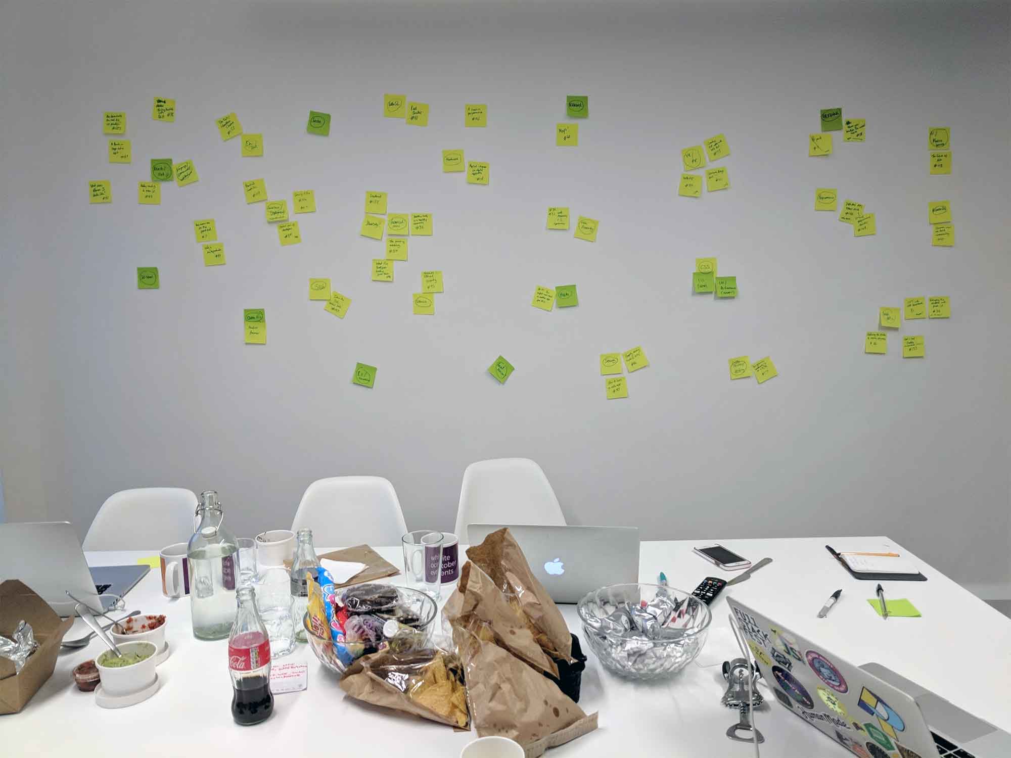 A wall of post-it notes in front of a table holding laptops and snacks